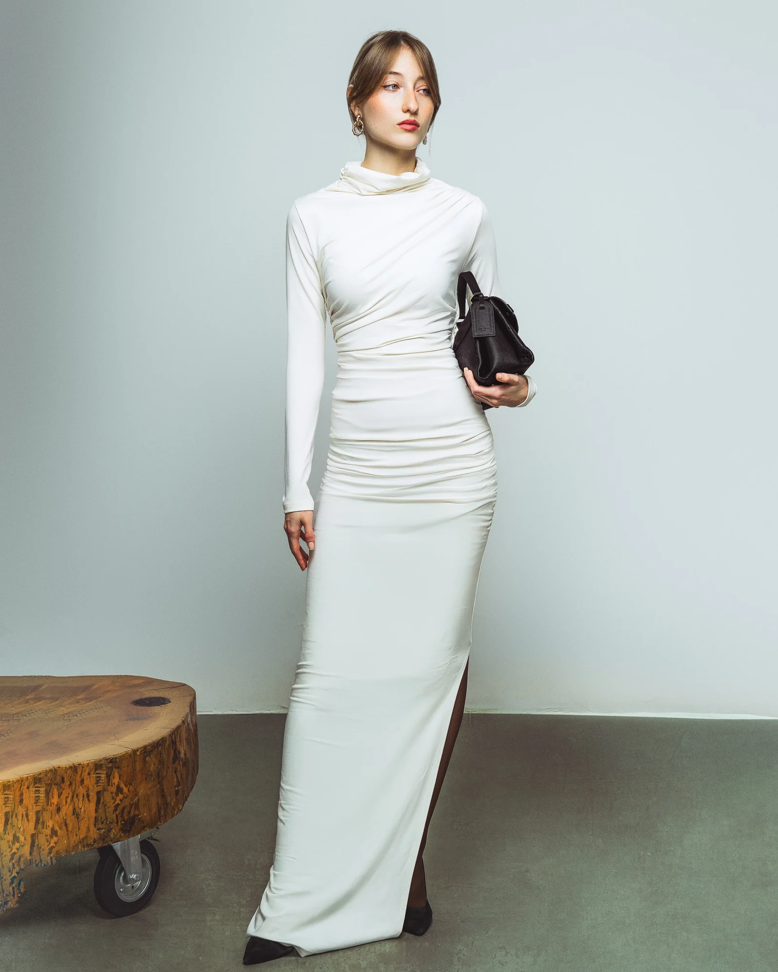 Incantevole Milano Fall Winter 2026–2027 – ivory long-sleeved draped gown beside a wooden table
