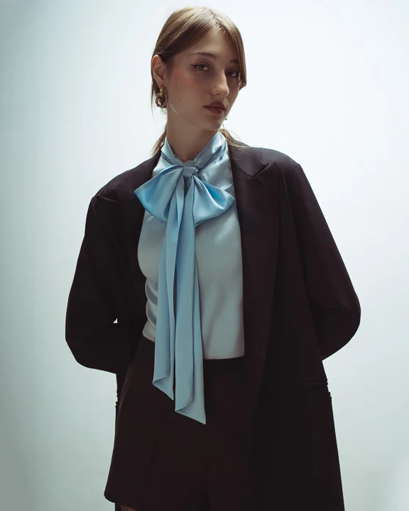 Incantevole Milano Fall Winter 2026–2027 – brown blazer and pale blue bow blouse in soft window light